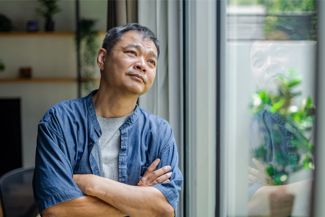 middle aged man day dreaming and looking through the window at home.
